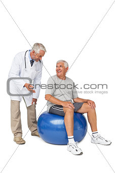 Male therapist looking at senior man sit on exercise ball