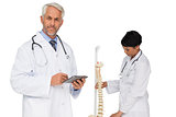 Doctor holding digital table with colleague by skeleton model