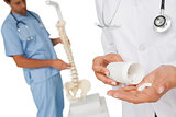 Mid section of female doctor with pills and skeleton model