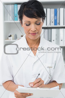 Concentrated female doctor writing on clipboard