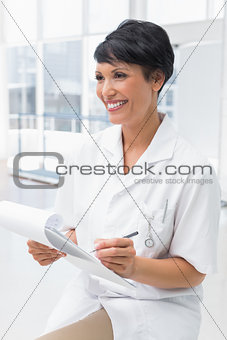 Smiling female doctor writing on clipboard