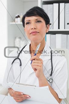 Thoughtful female doctor writing on clipboard