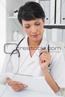 Concentrated female doctor writing on clipboard
