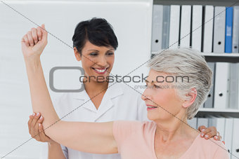 Physiotherapist assisting senior woman to stretch her hand