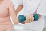Mid section of physiotherapist assisting woman to lift dumbbell