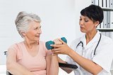 Physiotherapist assisting senior woman to lift dumbbell