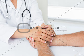 Close-up mid section of a doctor holding patients hands