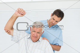 Male physiotherapist assisting senior man to raise hand