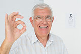 Smiling senior man gesturing ok with eye chart in background