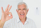 Smiling senior man gesturing ok with eye chart in background