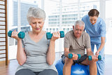 Female therapist assisting senior couple with dumbbells
