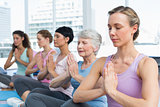 Class sitting with joined hands in a row at yoga class