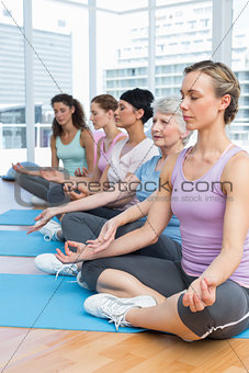 Women in lotus pose with eyes closed at fitness studio