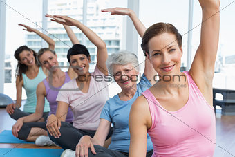 Trainer with women in row stretching hands at yoga class