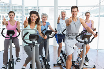 People working out at spinning class while gesturing thumbs up