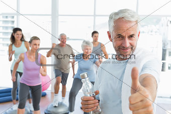 Senior man gesturing thumbs up with people exercising in fitness studio