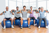 Fitness class with dumbbells sitting on exercise balls in gym