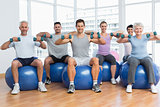 Fitness class with dumbbells sitting on exercise balls in gym