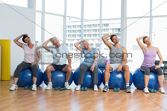 Class sitting on exercise balls and stretching neck in gym