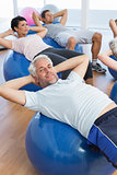 Smiling people stretching on exercise balls in gym