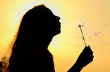 silhouette of girl blowing to dandelion