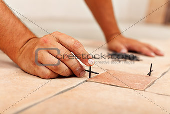 Worker hands placing spacers between ceramic floor tiles