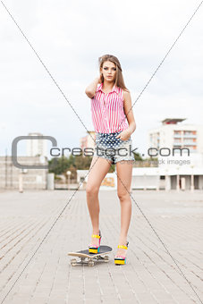 beautiful lady in short jeans shorts stands on skateboard