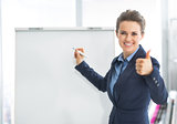 Smiling business woman near flipchart showing thumbs up