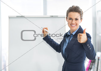 Smiling business woman near flipchart showing thumbs up