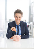 Smiling business woman putting coin into piggy bank