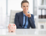 Closeup on piggy bank on table and happy business woman in backg