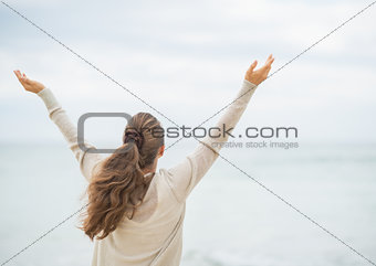 Young woman on cold beach rejoicing success. rear view