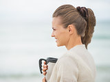 Happy young woman on cold beach with cup of hot beverage