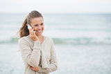 Smiling young woman talking cell phone on cold beach