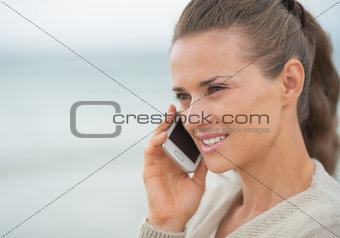 Young woman talking cell phone on cold beach