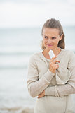 Thoughtful young woman with cell phone standing on cold beach