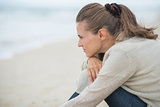 Calm young woman sitting on cold beach and looking into distance