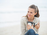 Relaxed woman sitting on cold beach with cup of hot beverage