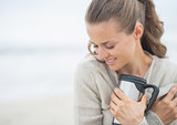 Portrait of relaxed woman sitting on cold beach with cup of hot 