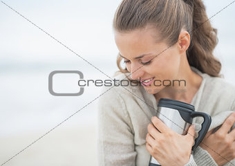 Portrait of relaxed woman sitting on cold beach with cup of hot 