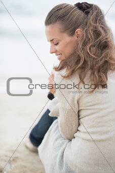 Happy woman sitting on cold beach. rear view