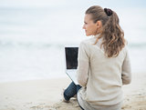 Young woman sitting with laptop on cold beach
