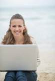 Happy young woman sitting with laptop on cold beach