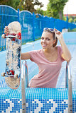 a beautiful young girl with a scateboard on the pool ladder 