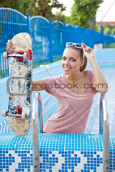 a beautiful young girl with a scateboard on the pool ladder 