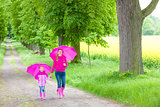 mother and her daughter with umbrellas in spring alley