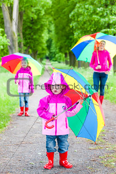 mother and her daughters with umbrellas in spring alley
