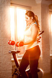 Woman at gym training with dumbbells at sunset