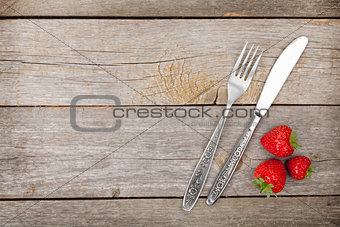 Ripe strawberries with silverware over wooden table background