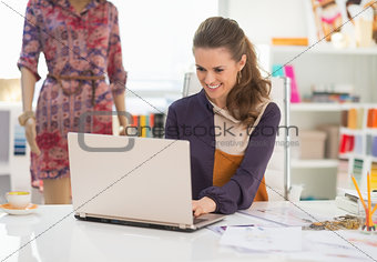 Happy fashion designer working on laptop in office